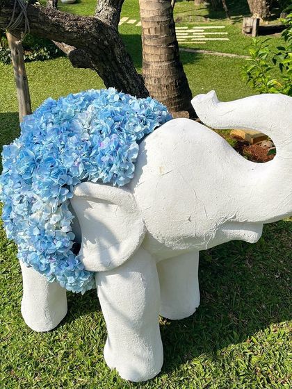 A single elephant statue covered in a blanket of blue hydrangeas, placed on the lush green lawn.