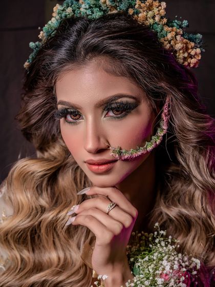 A stunning close-up of a floral-themed look. The makeup is soft and earthy, with a unique floral nose ring and crown made of dried flowers.
