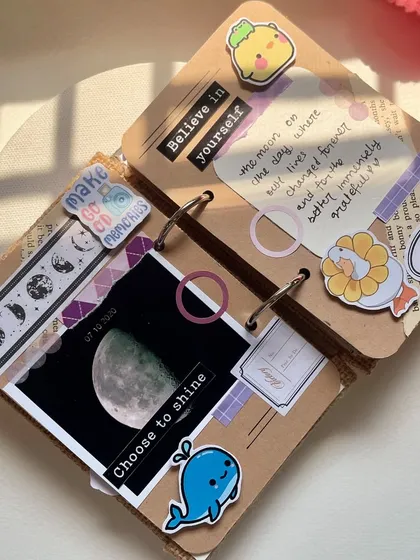 A peek inside one of my handmade scrapbooks. This page has a celestial theme, with a moon photo, space-themed washi tape, and a reminder to "Believe in yourself". Every page is fully customizable.