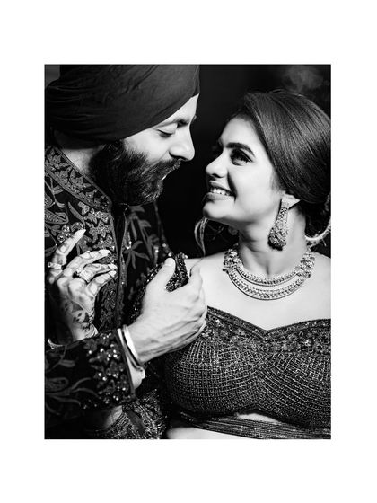 A classic black and white portrait capturing the loving gaze between the couple, highlighting the textures of their ornate outfits.