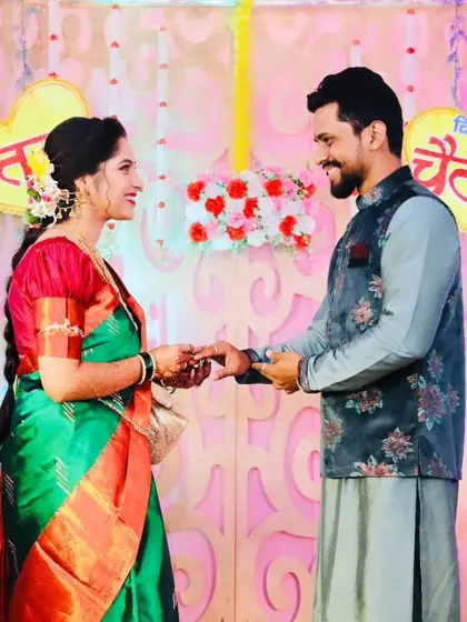 The ring exchange ceremony during an engagement. The bride looks radiant in her green and red saree, with makeup that highlights her joyful expression.