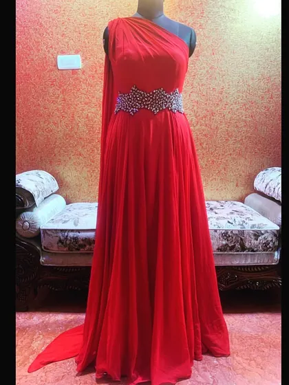 A show-stopping cocktail gown for a special occasion. This one-shoulder red gown features a flowing silhouette and a hand-embroidered belt made with semi-precious stones.