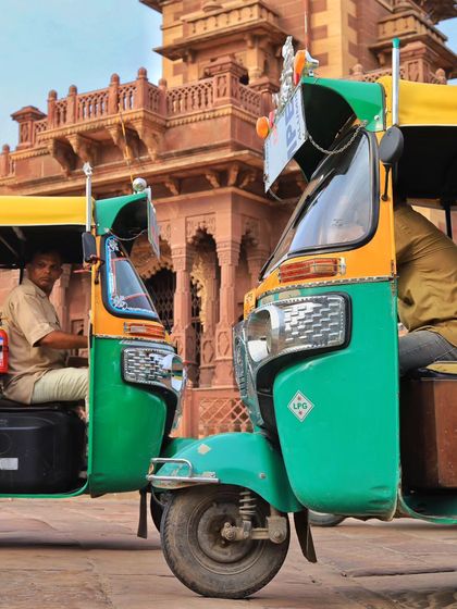 Two auto rickshaws parked symmetrically in front of traditional Rajasthani architecture. The vibrant green and yellow of the vehicles contrast beautifully with the stone building, telling a story without words.