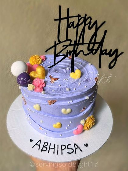 A cute lavender mini birthday cake with colorful hearts and flowers. It's a small cake that is big on charm.