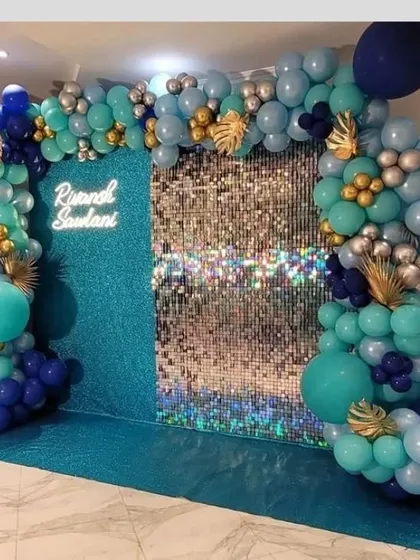 An ocean-themed party with a stunning turquoise and blue color palette. A silver sequin wall is framed by a balloon arch with gold leaf accents, creating a luxurious underwater feel.
