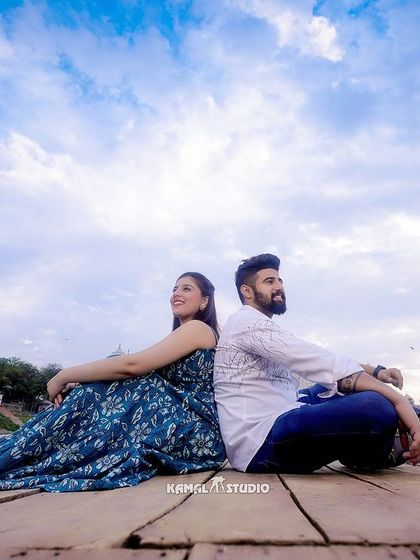 Sitting back-to-back on a boat deck, with the expansive sky and the distant monument creating a sense of shared dreams and a vast future together.