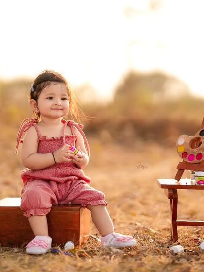 A toddler sits with a miniature easel and paint palette during an outdoor 'little artist' themed session at sunset.