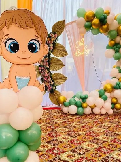 This 'Oh Baby' setup is perfect for a baby shower or welcome party. It features a large, cute baby character cutout on a balloon pillar, with a balloon ring arch and neon sign in the background.
