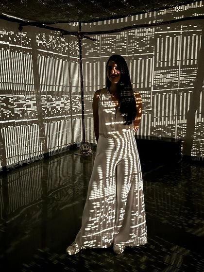 Artist Tanya Mehta posing within the 'WEAVING LIGHT' installation, her figure covered in the projected patterns.