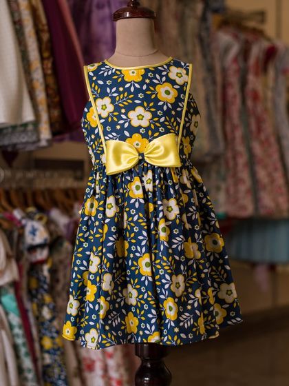 This navy blue dress is covered in a cheerful yellow and white floral print. A bright yellow bow at the waist makes the colors pop, creating a happy, sunny look.