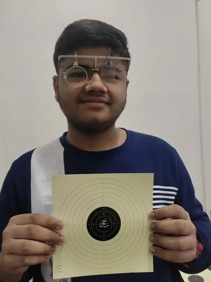 Ritvik, equipped with his shooting glasses, proudly holds up his 100/100 target. Proper gear is essential for achieving this level of precision.
