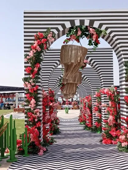 Symmetry, pattern, and blooms. This stunning entrance for a Doha celebration features a tunnel of black-and-white striped arches, lined with vibrant red flowers and quirky cactus props.