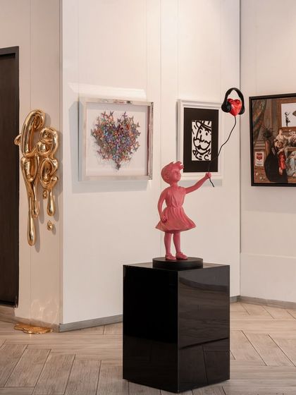 A corner of our gallery where playful sculptures and layered paintings coexist. The pink 'Girl with Balloon' sculpture offers a modern twist on a famous motif, while the surrounding artworks create a rich visual dialogue.