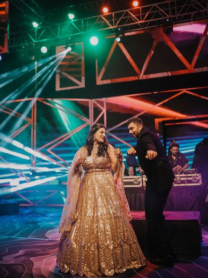 A candid moment on the Sangeet dance floor. The colorful stage lights and the couple's playful dance moves create a vibrant and energetic image that is full of life.