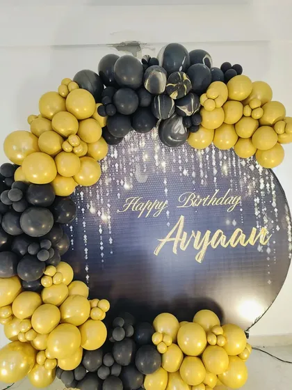 A close-up of a glamorous black and gold balloon arch against a custom printed backdrop with a sparkling light effect.