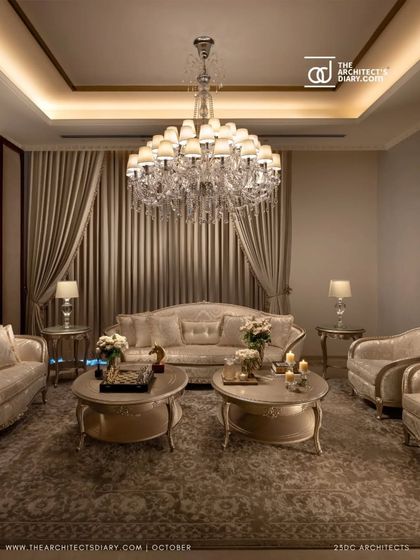 The formal living room of The Ivory Royale is bathed in the warm glow of a grand chandelier. The plush, classic sofas and soft carpeting create an inviting space that exudes opulence and comfort.