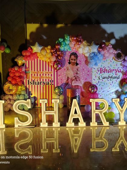 A sweet 'Candyland' theme for a fourth birthday party. This setup features large illuminated letters spelling the name, a custom candy-themed backdrop, and colorful balloon arrangements.