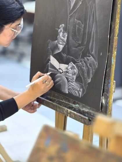 A close-up of the artist's hand as she works on the details of the book and hand in her portrait drawing.