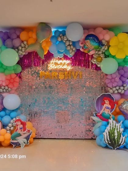 A Little Mermaid party with a sparkling sequin backdrop. This decoration features cutouts of Ariel, a marquee number '5', and a colorful balloon arrangement with mermaid tail and seashell accents.