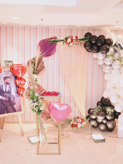 A personalized birthday setup showing a photo of the guest of honor on an easel, surrounded by romantic balloons and floral arrangements.