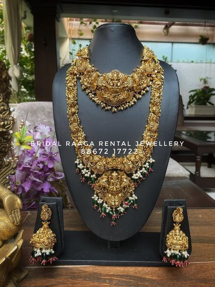 A classic temple jewellery set with a choker and long haram, both featuring Lakshmi pendants. The green and red bead droplets add a subtle touch of colour.