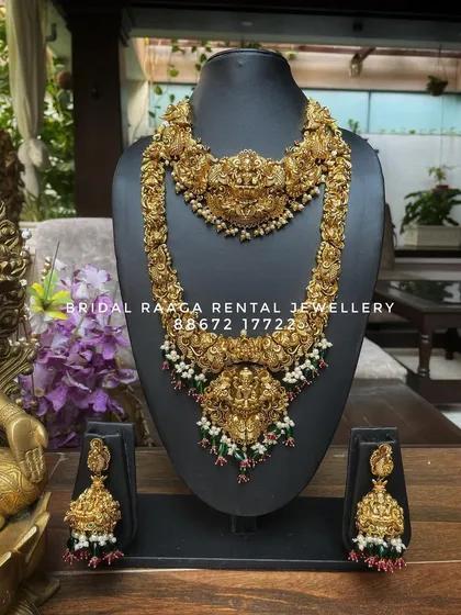 A classic temple jewellery set with a choker and long haram, both featuring Lakshmi pendants. The green and red bead droplets add a subtle touch of colour.
