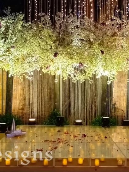 A dance floor ready for the celebration. The stage is framed by illuminated cherry blossom trees and a backdrop of stone walls, with a mirrored floor reflecting the lights from above.