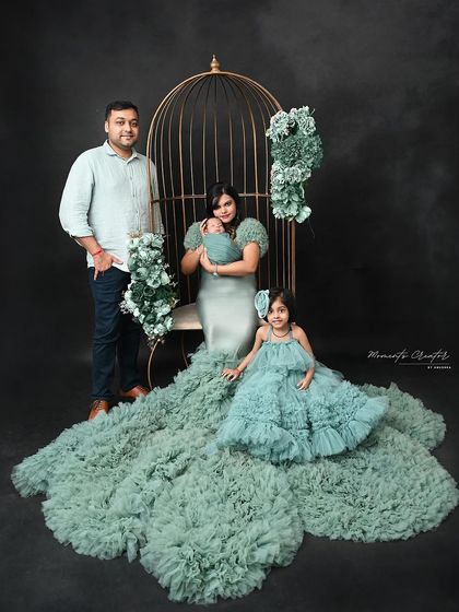 An elegant family of four portrait. The mother and daughter wear stunning matching green gowns, creating a sophisticated and memorable image with their newborn baby.