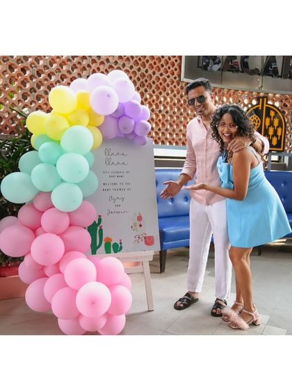 The happy couple at their "Taco Bout a Baby" themed shower. The welcome sign is framed by a vibrant pastel balloon arch, setting a fun and festive tone.