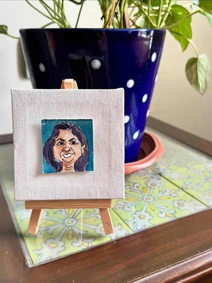 My mini portrait of Sharda displayed on an easel, next to a plant.