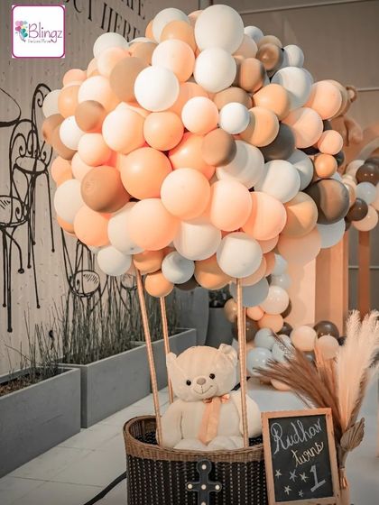 An adorable teddy bear sits in a hot air balloon made of balloons. This creative and cute prop was a highlight of a teddy bear themed first birthday, perfect for photos and adding a whimsical touch.