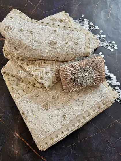 We present our heirloom Chikankari saree, a testament to opulent craftsmanship. Rendered on off-white crepe, this made-to-order piece is heavily highlighted with mirrorwork, Kutdana, and sequins, and is styled here with a complementary clutch for a complete festive look.