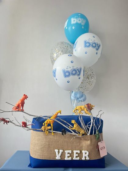 A wild welcome for baby Veer! This jungle-themed hamper features a personalized name, animal figures, and a blue and white balloon bouquet.
