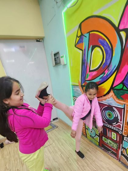 Stretching can be fun too. Our young dancers help each other with leg holds and kicks, building both flexibility and teamwork in the process.