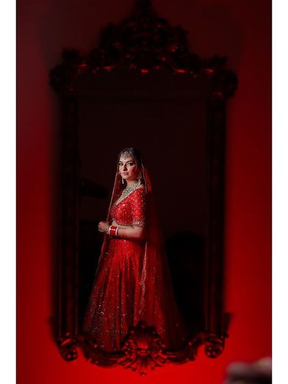 A dramatic bridal portrait, with the bride in red reflected in a large, ornate mirror against a red wall.