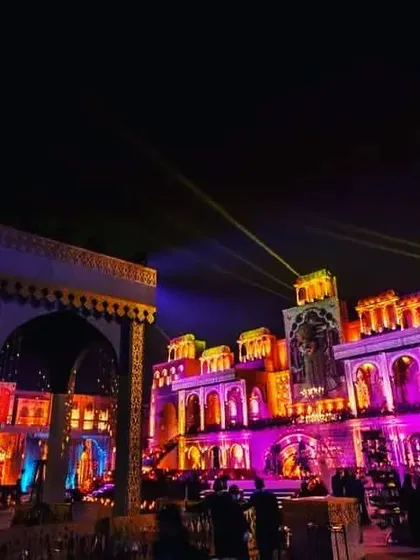 An exterior view of a massive, multi-colored palace set created for a sangeet. The use of projection mapping and vibrant lights transformed the structure into a dynamic canvas of color.