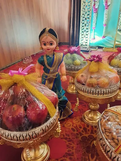 Our traditionally dressed dolls add a charming touch to the platter display. Here, a doll stands beside platters of fresh apples and other fruits, all neatly wrapped for the ceremony.