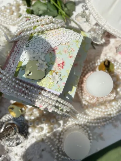 A close-up of the intricate details from the Bridgerton theme, including custom stationery with lace and heart-shaped locks, surrounded by pearls and candles.