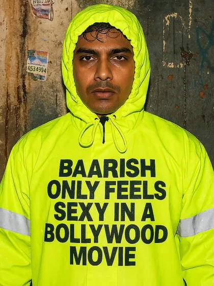 A man in a neon green raincoat that reads 'BAARISH ONLY FEELS SEXY IN A BOLLYWOOD MOVIE'. This 'Rainquotes' piece punctures a popular romantic myth with a dose of reality.