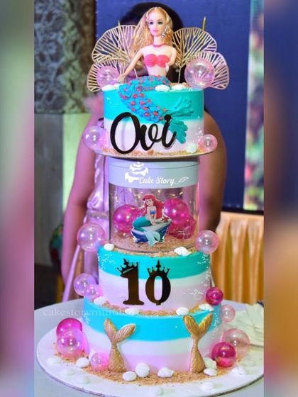 A grand mermaid-themed rotating cake for a 10th birthday. This three-tier creation features a Barbie mermaid, bubble decorations, and golden mermaid tails.