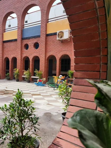 A view of the school courtyard through a brick archway, creating a beautiful frame for the playful and colorful environment within. The design uses classic architectural elements to create a sense of rhythm and order.