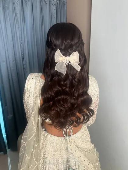 The back of this romantic half-up hairstyle. The soft waves are accented with a delicate white bow, adding a touch of modern femininity.