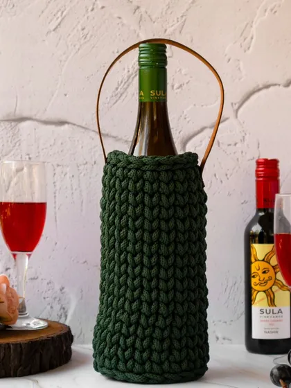 A close-up of the hand-crocheted wine bag in a festive setting. The rich green of the bag complements the red wine, creating an elegant and celebratory feel.