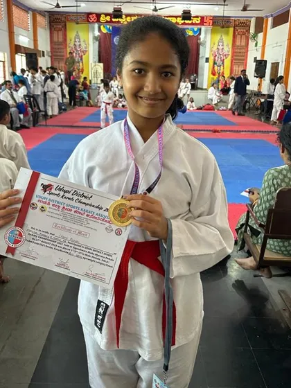 A red-belt student proudly displays her gold medal after a successful competition.