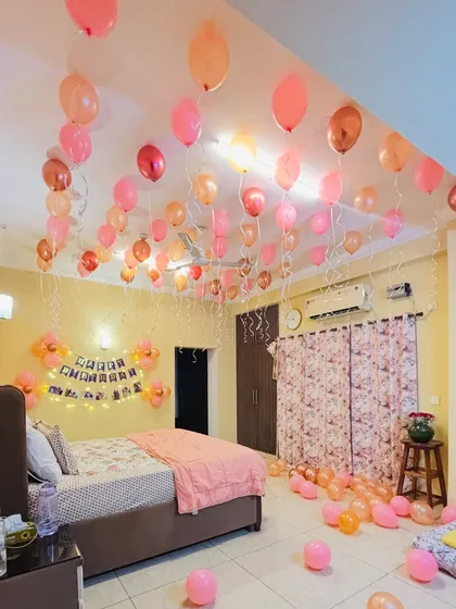 A simple and sweet birthday room decoration with dozens of pink and peach balloons floating on the ceiling and scattered on the floor.