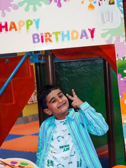 A happy birthday boy poses in the art-themed photo frame, showing off his peace sign and big smile.