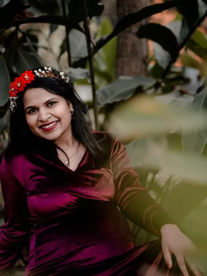 A candid shot of a smiling mom-to-be in a rich velvet dress, framed by lush green leaves. We look for these natural frames in the environment to create beautiful, intimate portraits.