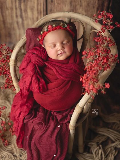 A close-up on the baby's face, showing the delicate, custom-made headband that perfectly complements the deep red theme.