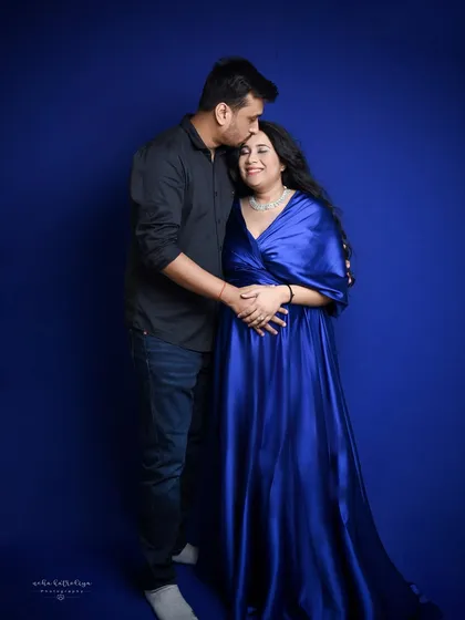 This portrait uses a bold, royal blue backdrop that makes the couple stand out. The flowing satin gown adds a touch of glamour to the maternity shoot.