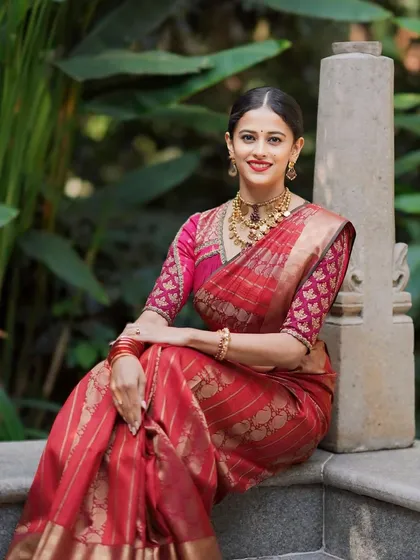 A client looking elegant in a red Banarasi silk saree. Her custom blouse features a brocade pattern and simple gold embroidery, a classic and timeless combination.